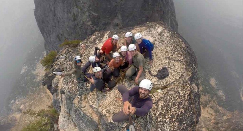 a group of people wearing rock climbing gear smile at the top of a summit